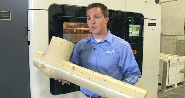Kyle Whitlow, ingénieur chez ULA tient le système de conditionnement imprimé en 3D à l'aide de la Fortus 900mc (en arrière plan).